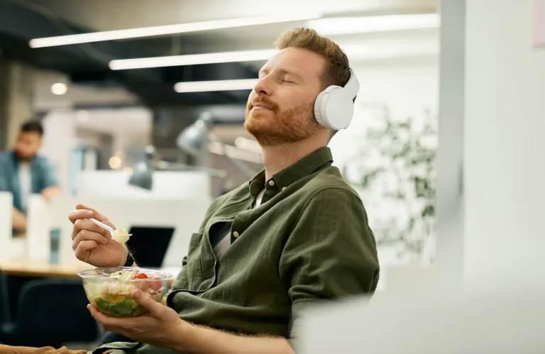 Büro-Mitarbeiter macht Mittagspause im Büro und genießt entspannt Musik über Kopfhörer.