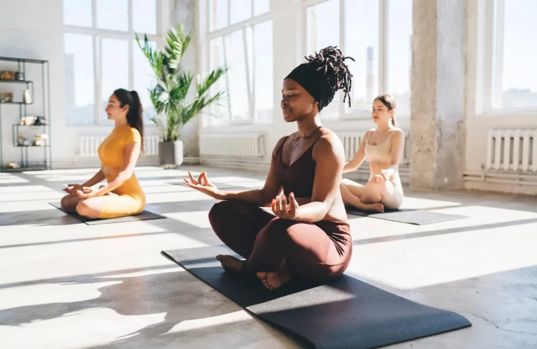 Eine Gruppe von Frauen meditiert während einer Yoga-Stunde in einem hellen Studio.