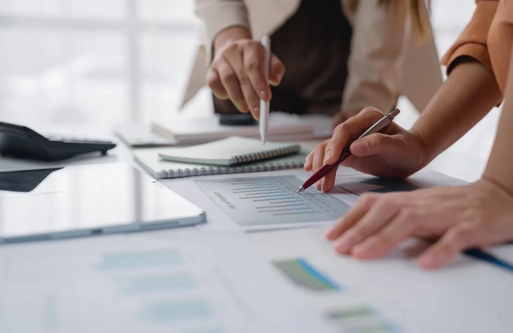 Geschäftsleute analysieren im Büro gemeinsam Finanzdiagramme mit Stiften, Taschenrechnern und Tablets für die Wachstumsplanung.