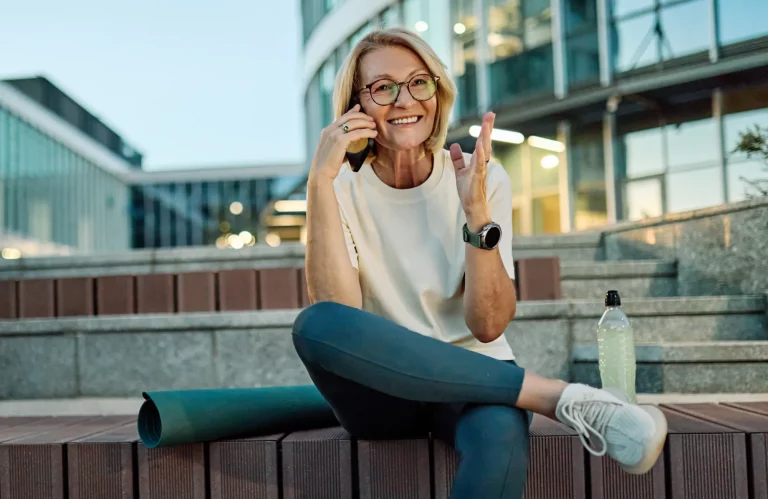 Sportliche Frau mittleren Alters telefoniert gut gelaunt auf ihrem Smartphone.