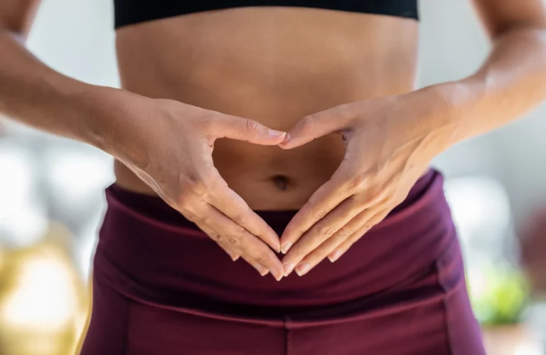Sportliche Frau bildet mit ihren Händen ein Herz auf ihrem Bauch als Symbol für Darmgesundheit und Körperliebe.