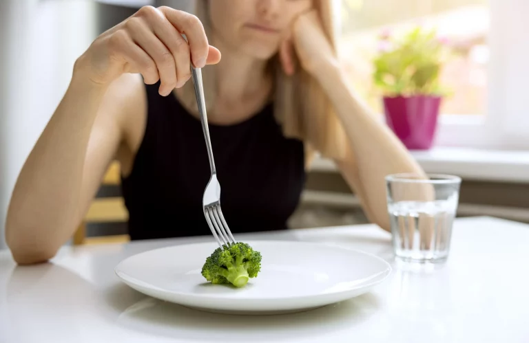Eine deprimiert Frau blickt auf eine sehr kleine Portion Brokkoli auf ihrem Teller.