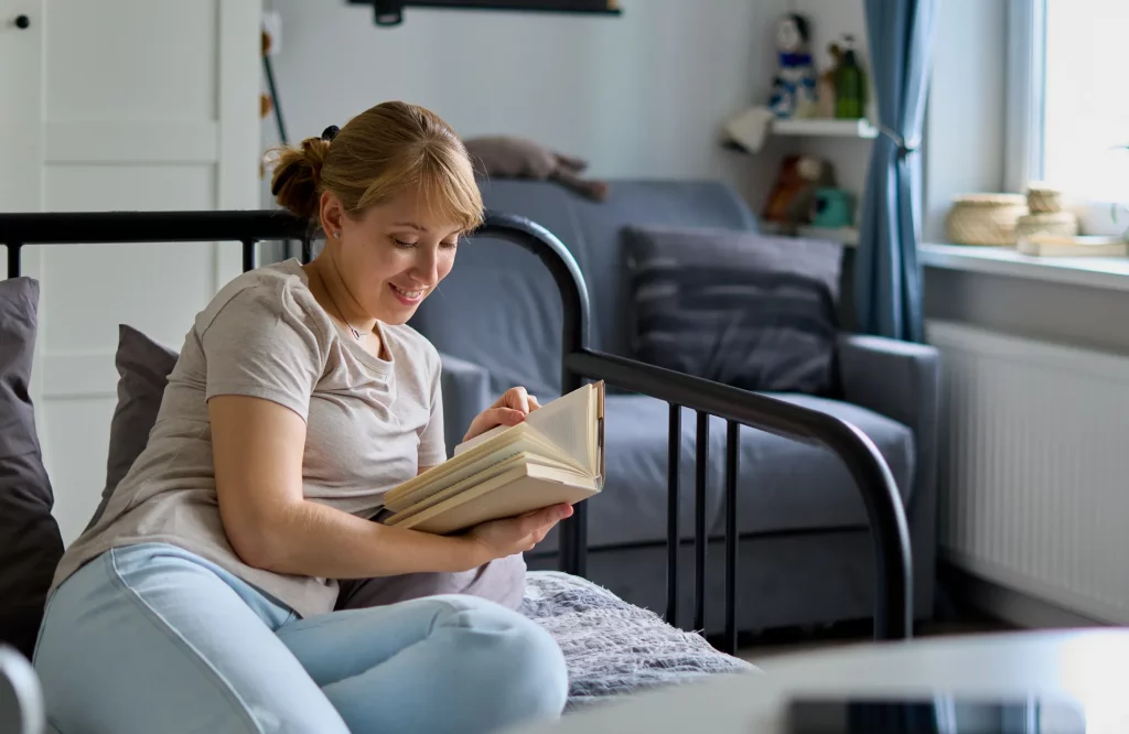 Eine lächelnde Frau liest entspannt ein Buch auf dem Bett.