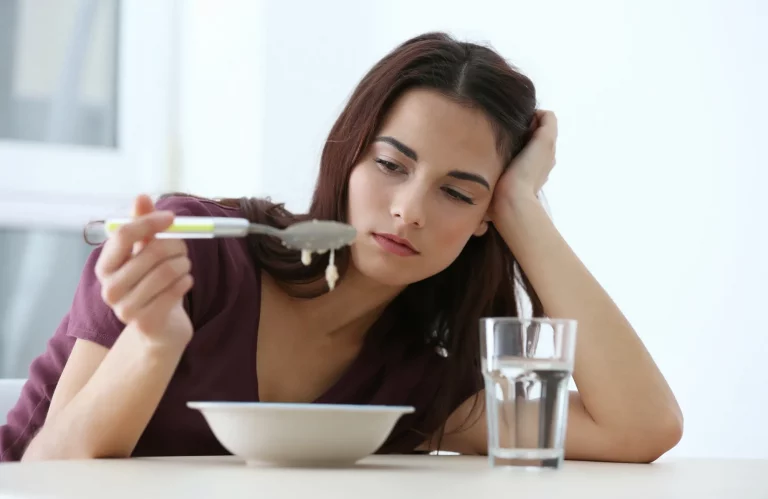 Frau sitzt appetitlos am Küchentisch und lässt lustlos die Suppe vom Löffel tropfen als Zeichen von Unwohlsein oder Stress.