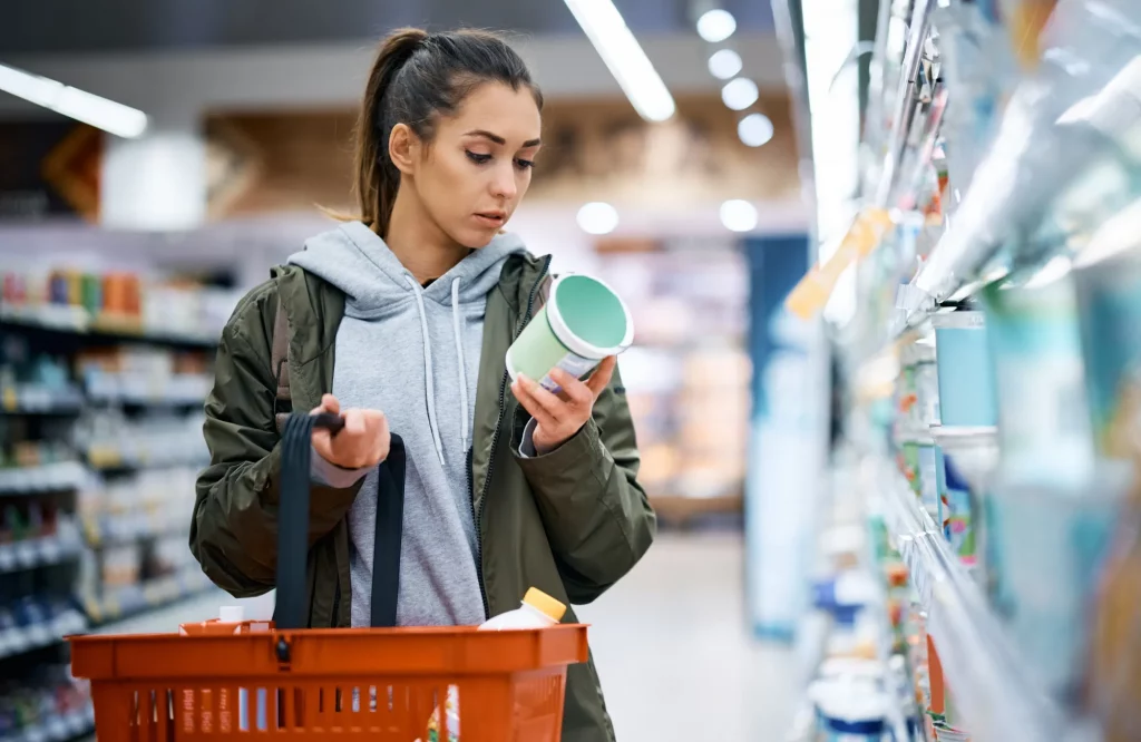 Eine Frau liest im Supermarkt aufmerksam das Etikett eines Milchprodukts.