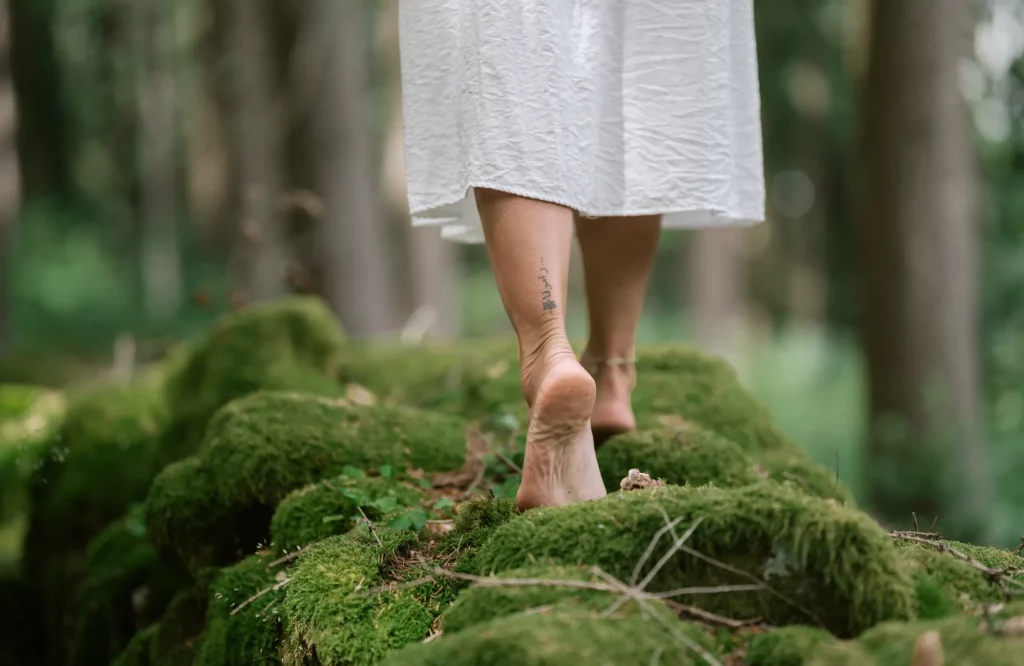 Nahaufnahme von weiblichen Füßen, die barfuß über moosigen Boden in einem ruhigen Wald gehen.