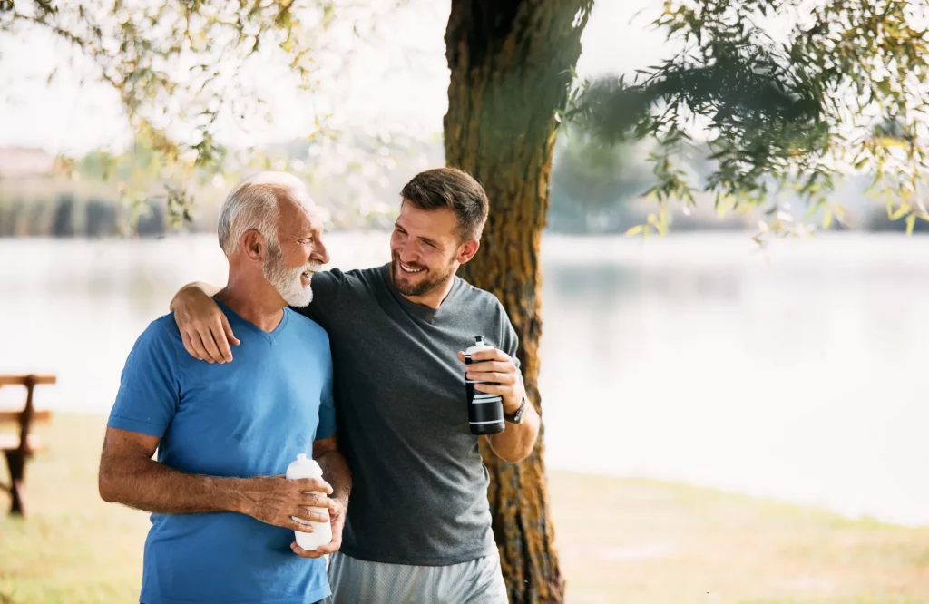 Zwei Männer unterhalten sich nach dem Sport in der Natur und trinken Wasser.