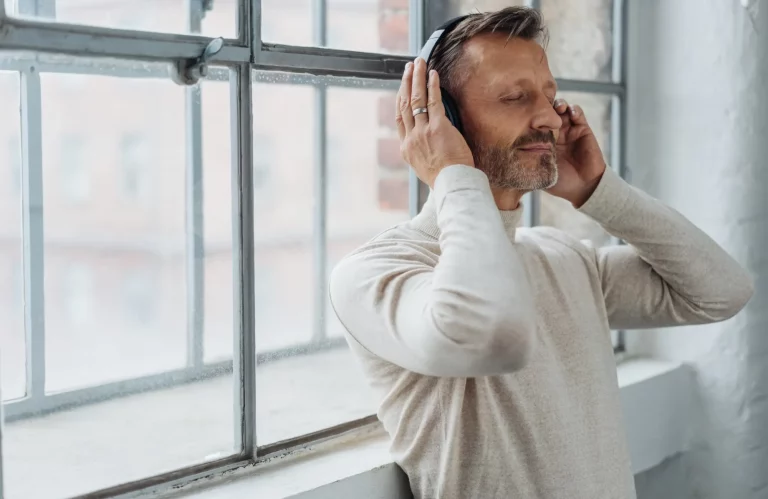 Ein Mann hört entspannt Musik und lehnt dabei an einem Fenster.
