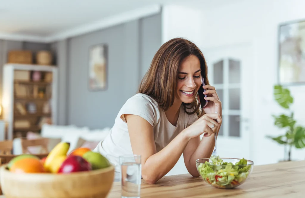 Eine lächelnde Frau isst einen frischen Salat, während sie telefoniert.