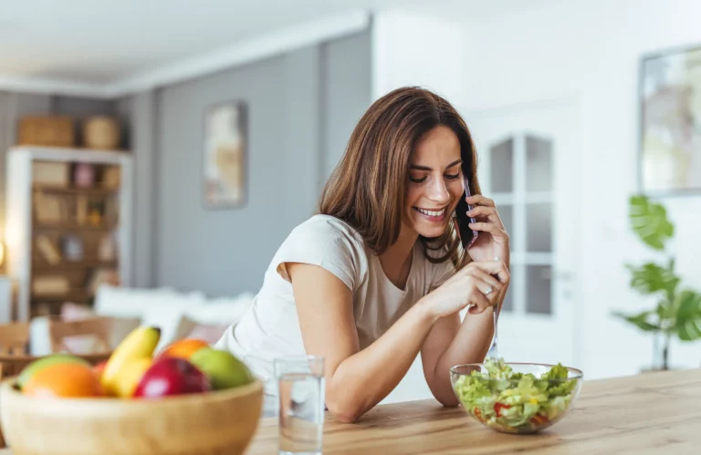 Eine lächelnde Frau isst einen frischen Salat, während sie telefoniert.
