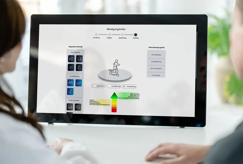 GiB-Trainer und Teilnehmerin beim digitalen Bewegungsindex an einem Touch-Display.