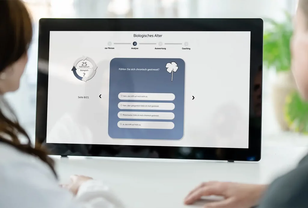 GiB-Trainer und Teilnehmerin beim digitalen Biologischen Alter an einem Touch-Display.