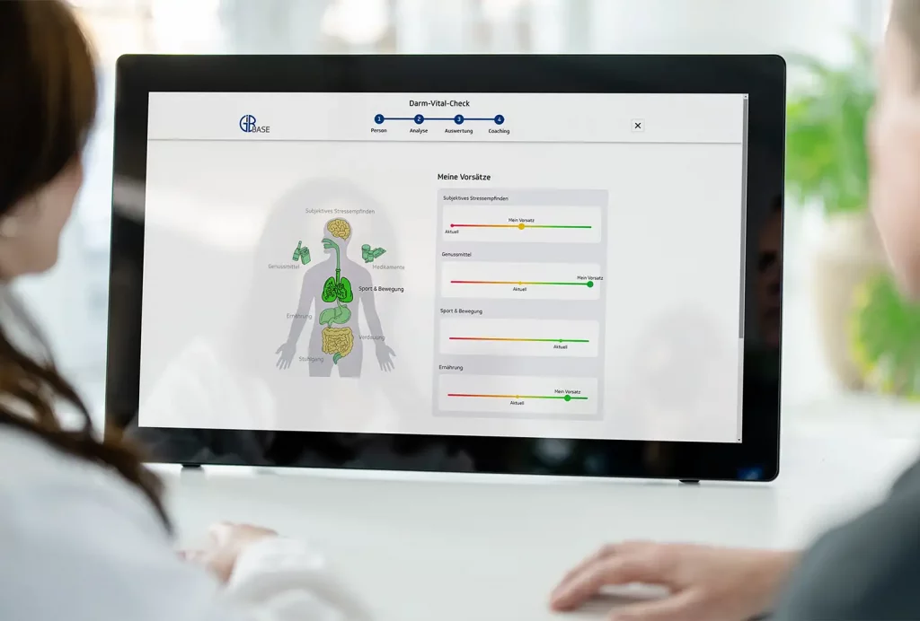 GiB-Trainer und Teilnehmerin beim digitalen Darm-Vital-Check an einem Touch-Display.