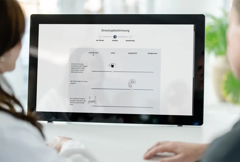 GiB-Trainer und Teilnehmerin bei der digitalen Stresstypbestimmung an einem Touch-Display.