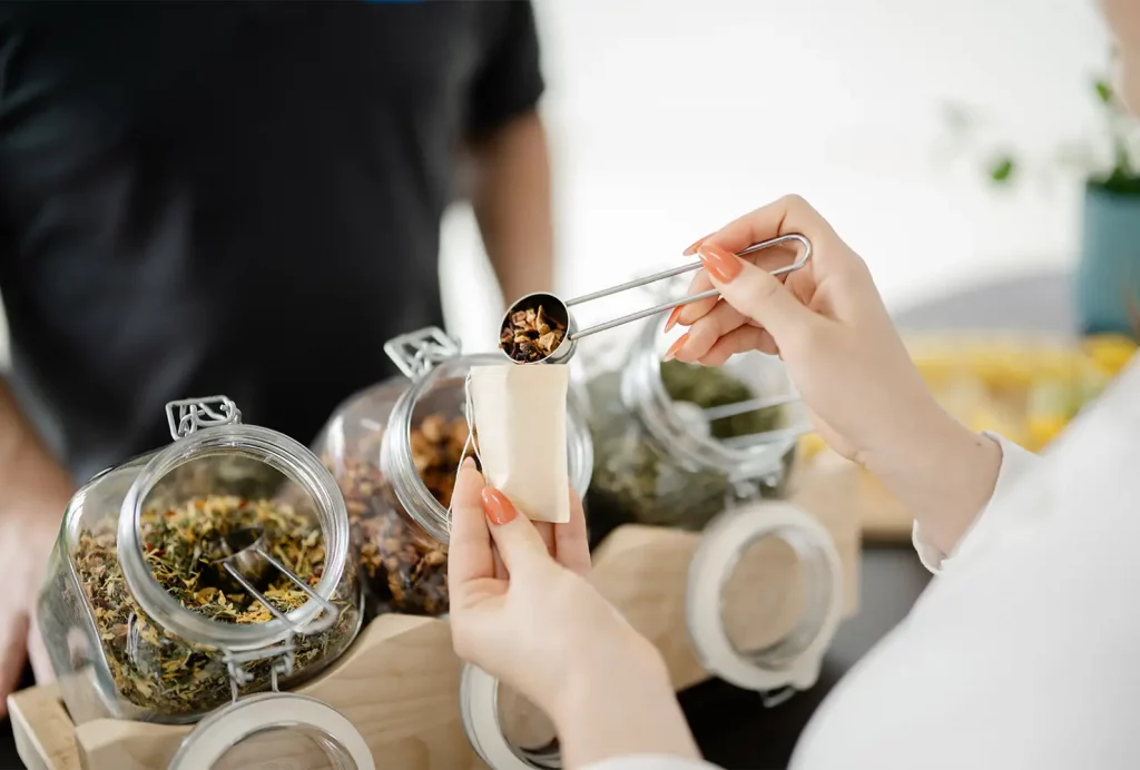Nahaufnahme einer Teilnehmerin, die sich ihre individuelle Teemischung aus getrockneten Teeblättern für die Zubereitung von Infused Tea zusammenstellt.