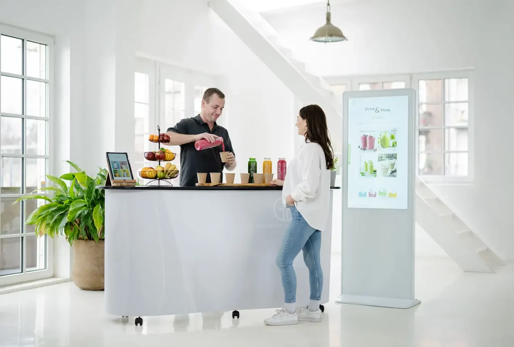 GiB-Trainer reicht einer Teilnehmerin am interaktiven „Drink & Think“-Stand eine frische Smoothie-Probe zur Verkostung.