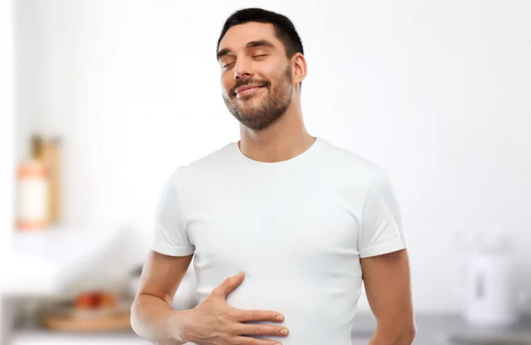 Ein Mann steht in der Küche und hält sich zufriedener mit einer Hand den Bauch.