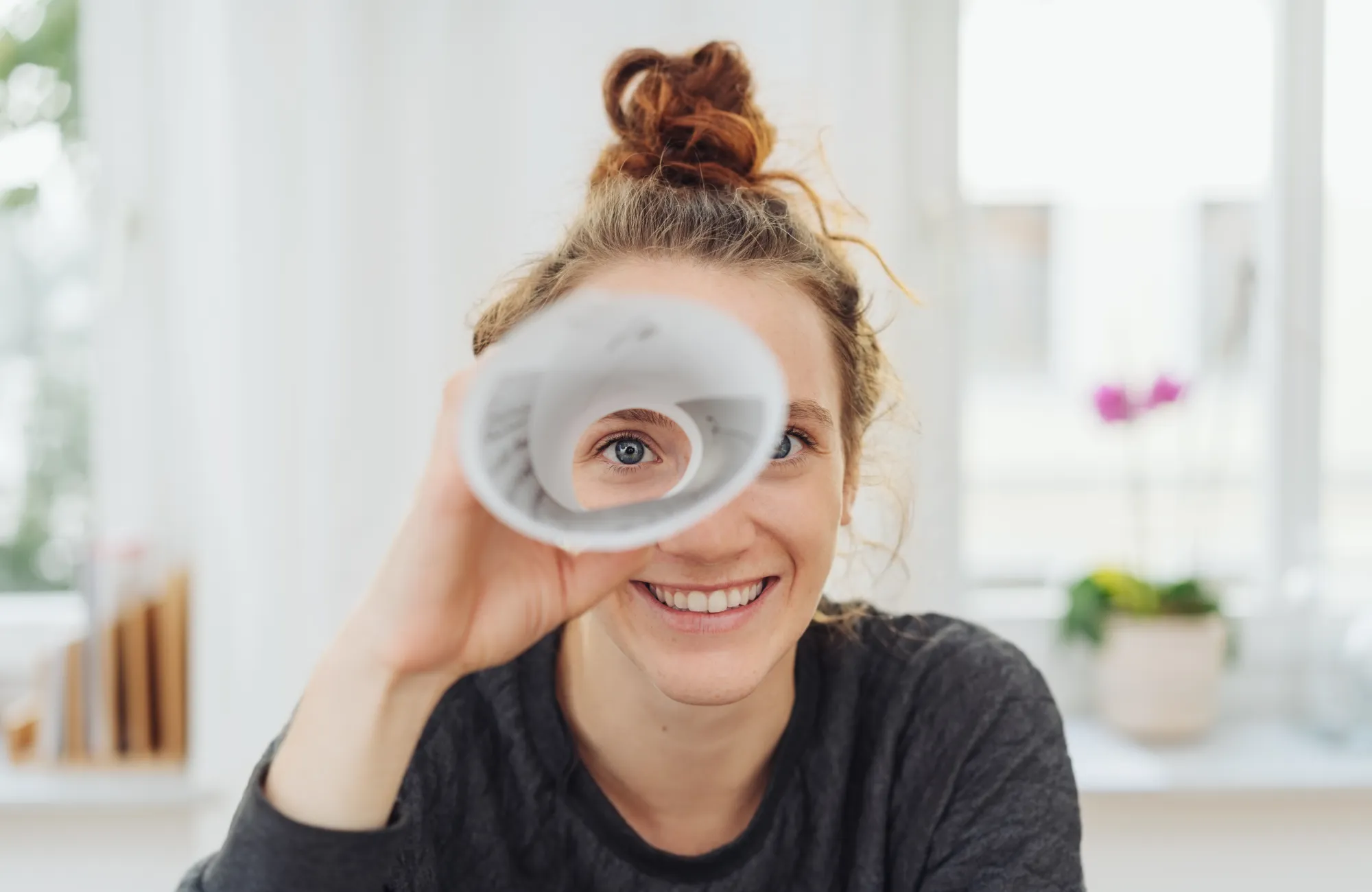 Lachende junge Frau schaut optimistisch durch ein Fernrohr aus Papier – Symbol für neue berufliche Perspektiven und Karrierechancen.