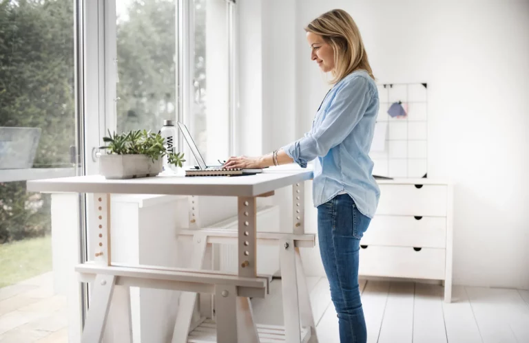 Frau arbeitet an einem ergonomischen Stehschreibtisch im Büro.
