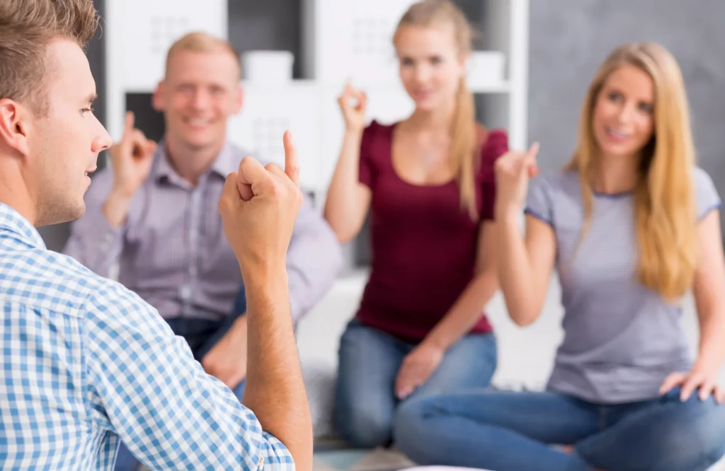 Eine Gruppe Erwachsener sitzt im Kreis auf dem Boden und führt gemeinsam eine Finger-Koordinationsübung zur Steigerung der Konzentration aus.