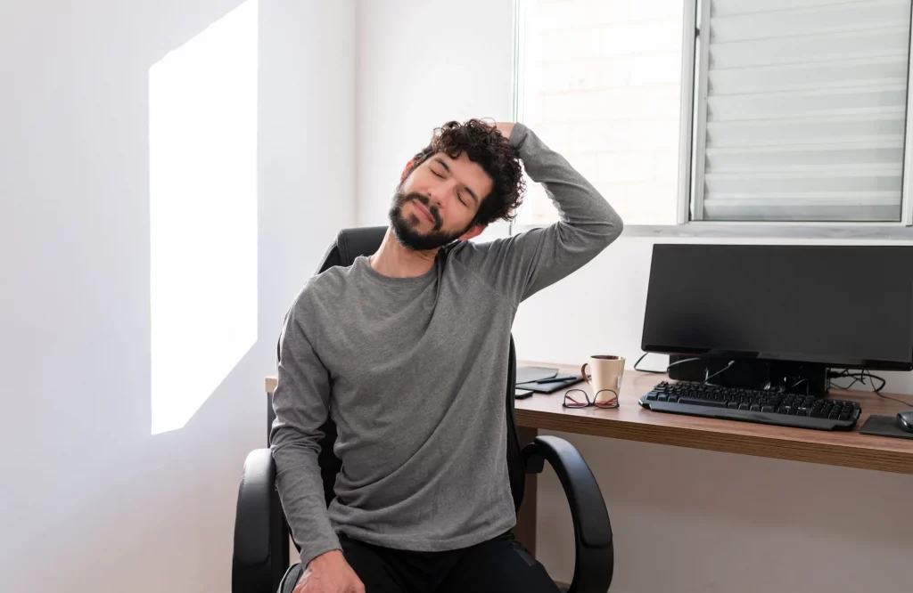 Ein Mann im Homeoffice dehnt sich während der Arbeitspause in seiner Wohnung.