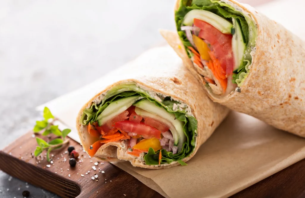 Ein veganer Wrap, gefüllt mit knackigem Gemüse, halbiert auf einem Brett serviert.