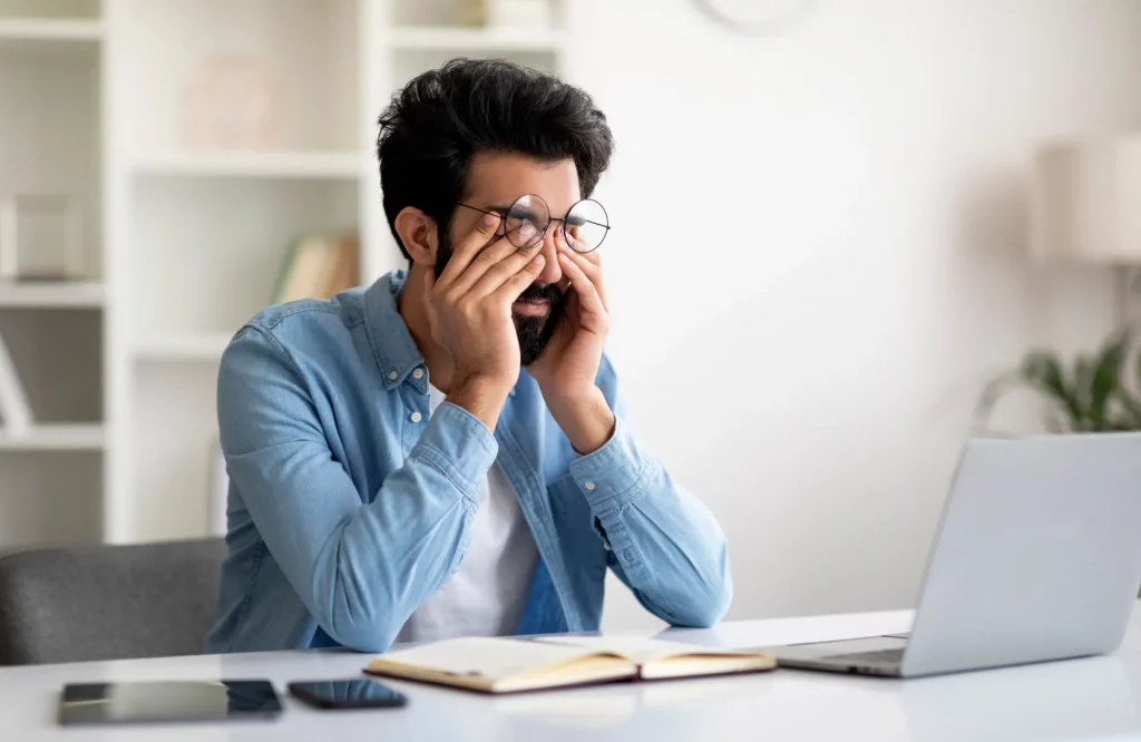 Mann massiert sich am Schreibtisch die müden Augen nach der konzentrierten Arbeit am Laptop.
