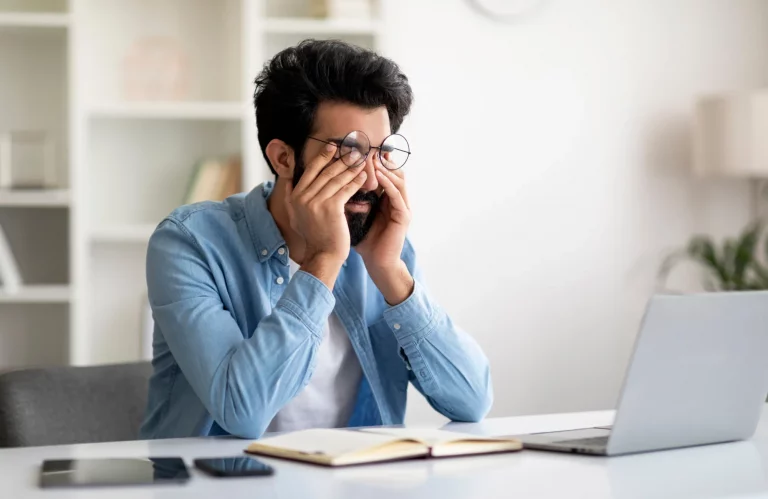 Mann massiert sich am Schreibtisch die müden Augen nach der konzentrierten Arbeit am Laptop.