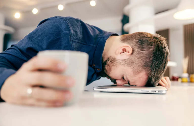 Erschöpfter Mann schläft bei der Arbeit mit dem Kopf auf der Laptop-Tastatur ein.