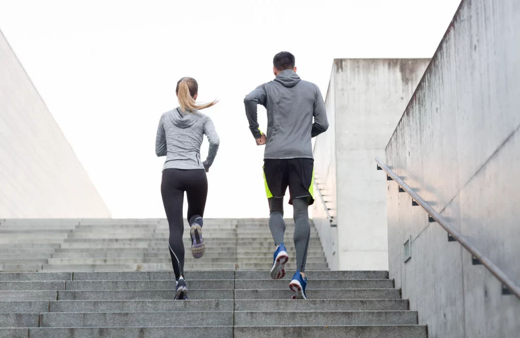 Frau und Mann beim gemeinsamen Lauftraining auf einer Treppe im städtischen Bereich.