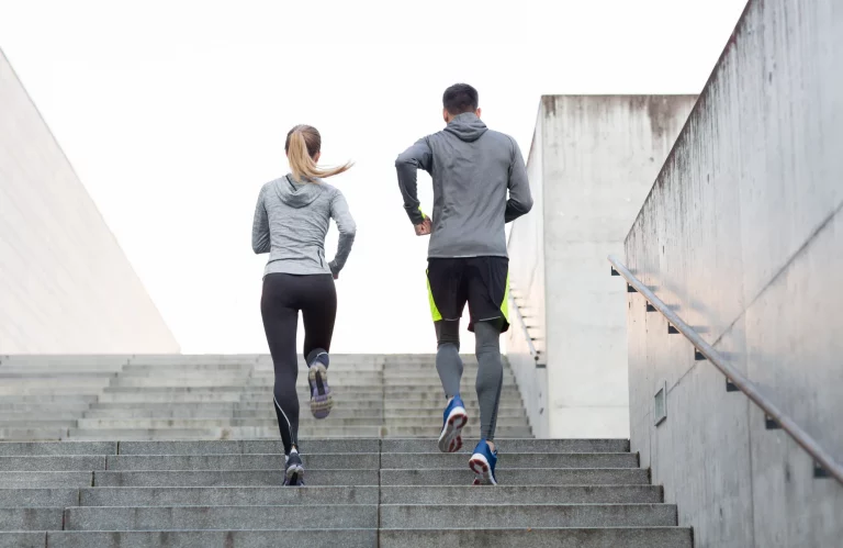 Frau und Mann beim gemeinsamen Lauftraining auf einer Treppe im städtischen Bereich.