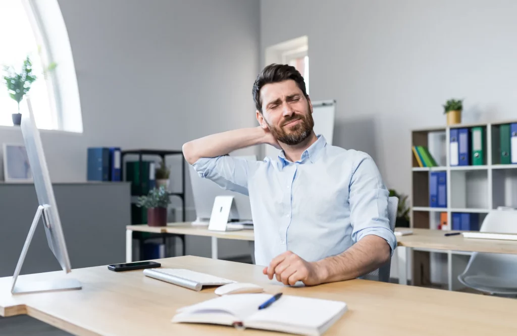 Ein Mann hält sich bei der Arbeit schmerzend den Nacken.