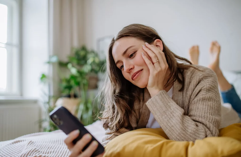 Eine Frau liegt auf dem Bett und nutzt ihr Smartphone.