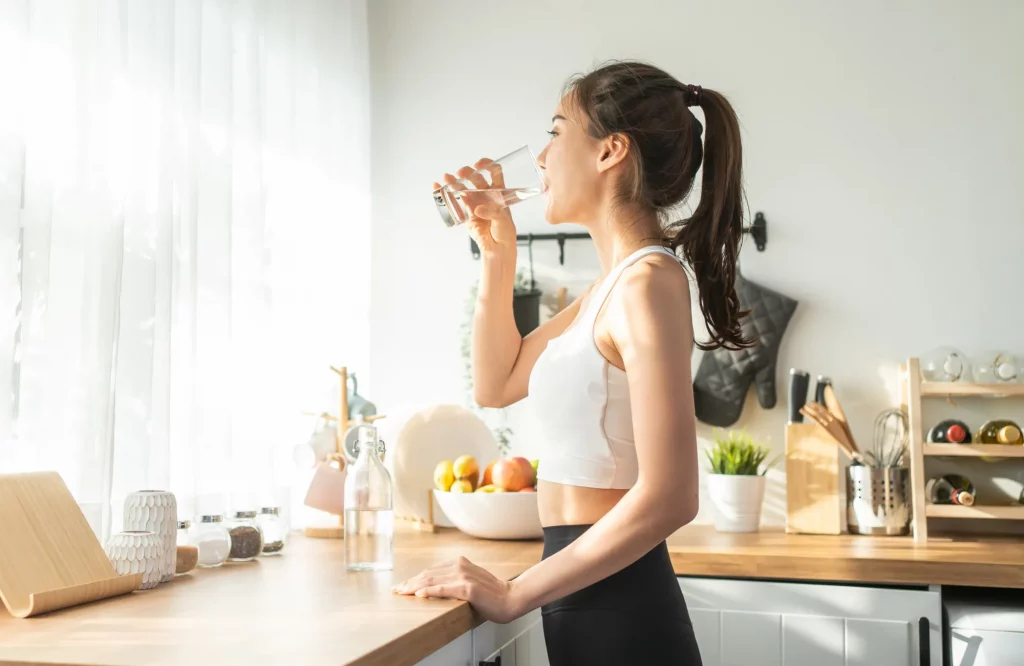 Eine Frau in Sportkleidung trinkt zu Hause Wasser aus einem Glas.