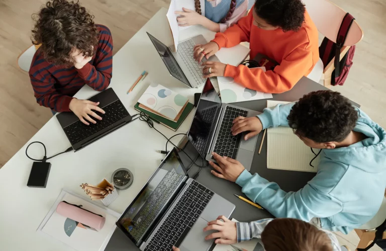 Draufsicht auf eine Gruppe von Azubis, die gemeinsam an Laptops lernen.