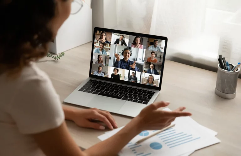Rückansicht einer Auszubildenden, die im Homeoffice an einer virtuellen Team-Besprechung am Monitor teilnimmt.