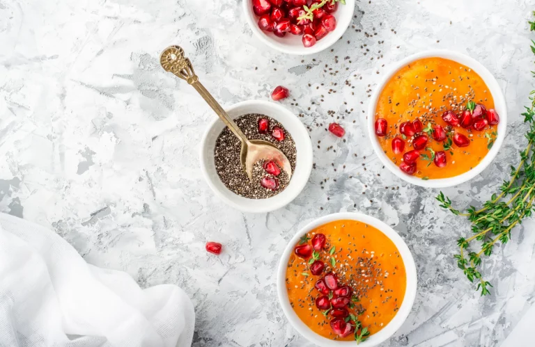 Draufsicht auf ein Frühstück mit saisonalen Früchten, Milch, Chia-Samen und Granatapfelkernen auf Marmor.