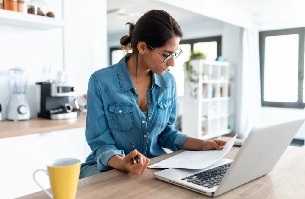 Eine Frau arbeitet in der Küche mit Unterlagen und einem Laptop.